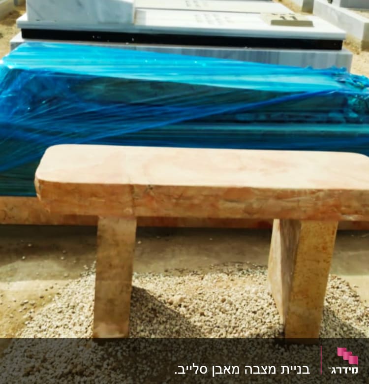 קבר מכוסה בניילון כחול עם ספסל אבן מלפנים